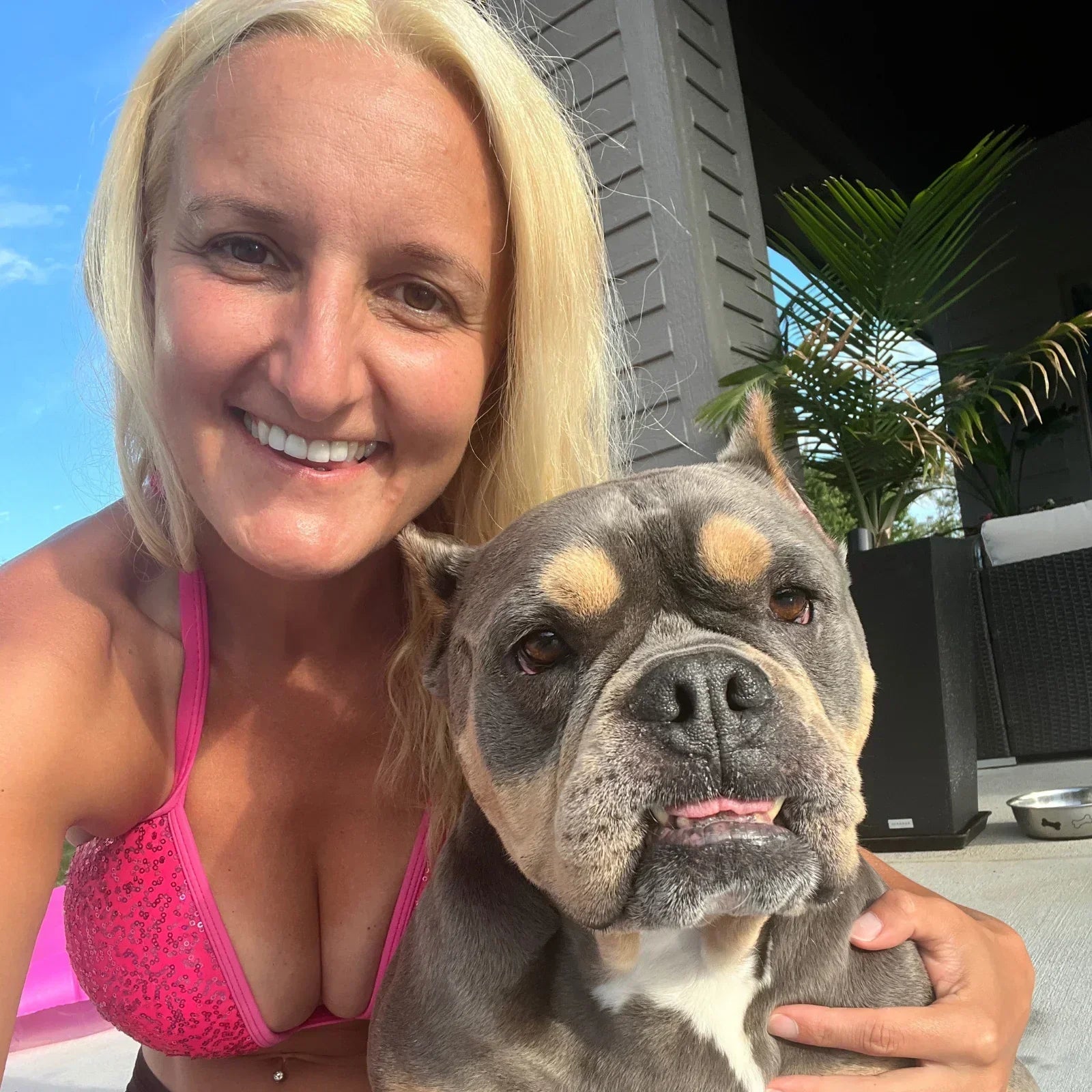 Dog mom wearing a pink swimsuit sitting with her American Bully dog enjoying summer.