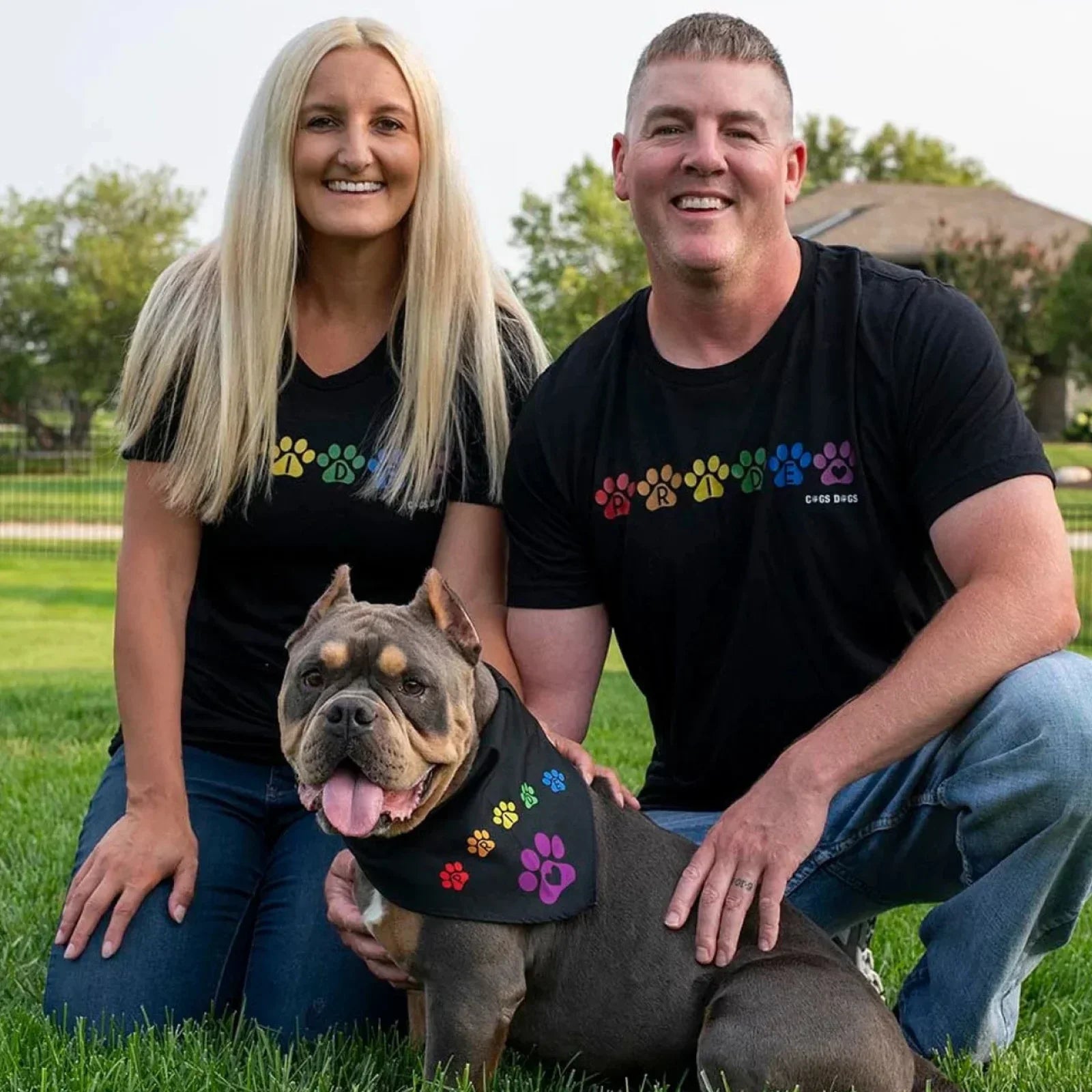 Dog mom and dog dad sitting with their dog all wearing matching Pride Rainbow t-shirts & bandana.