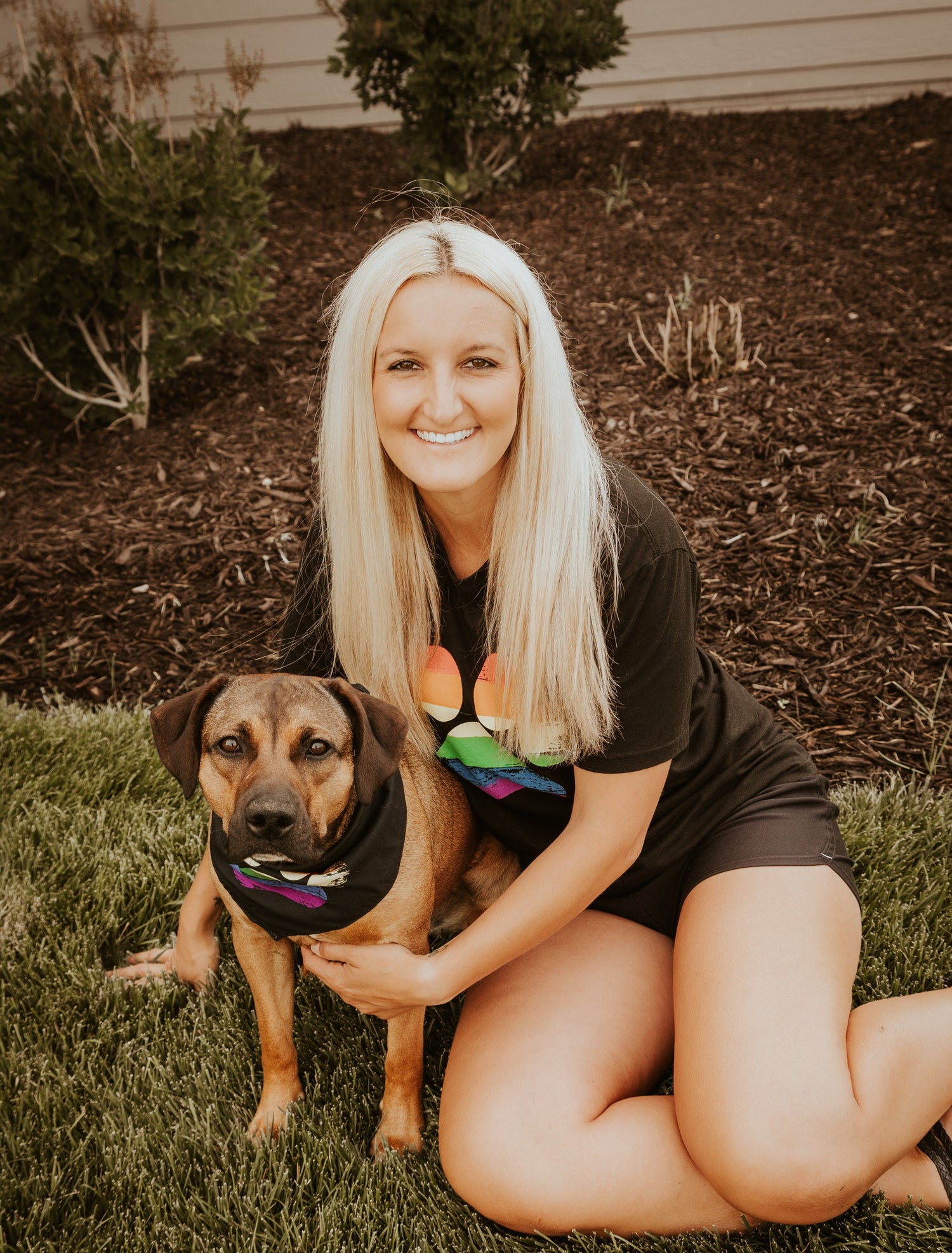 Woman sitting on grass with a dog wearing a rainbow bandana